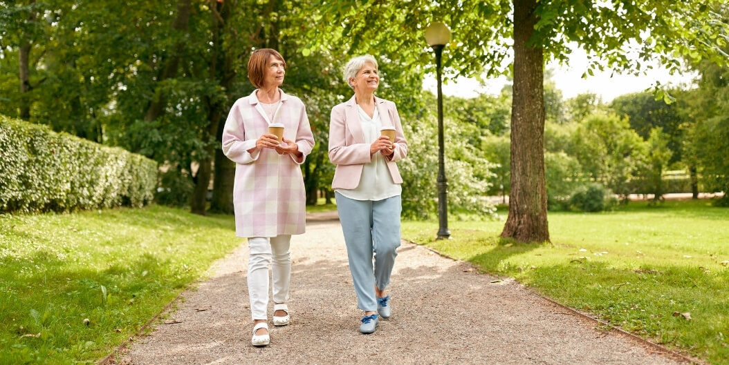 Elderly Women Walking With Coffee in Park in Independent Living