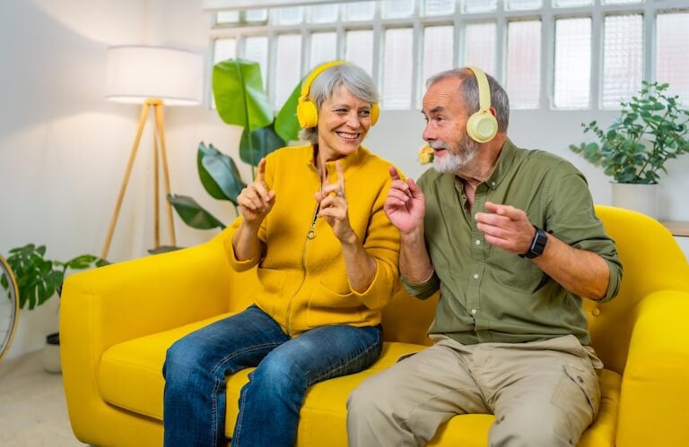 Elderly Couple Wearing Headphones Dancing on a Yellow Sofa at an Independent Living Community